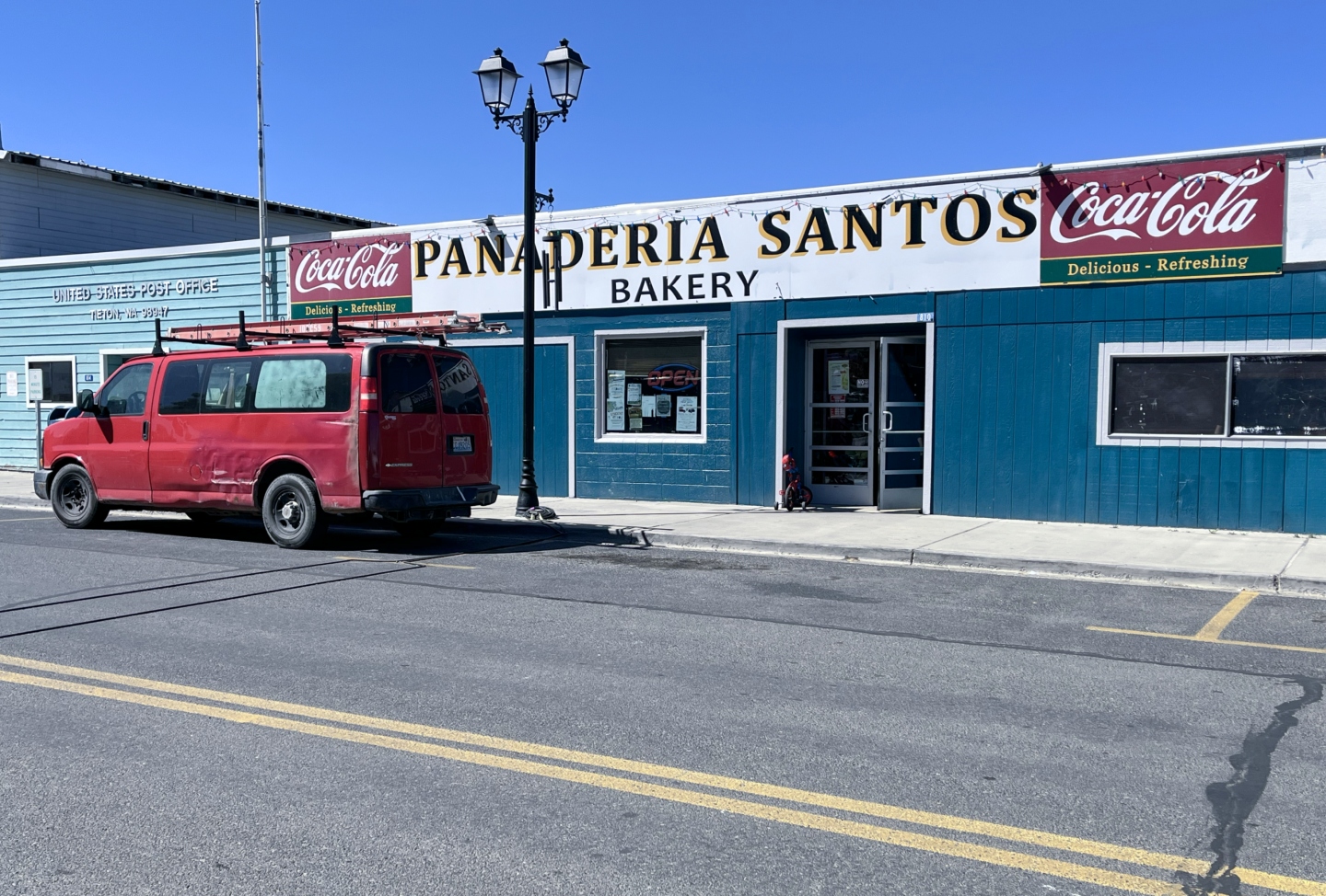 Photo of single story blue bakery storefront, with red worker truck on left.