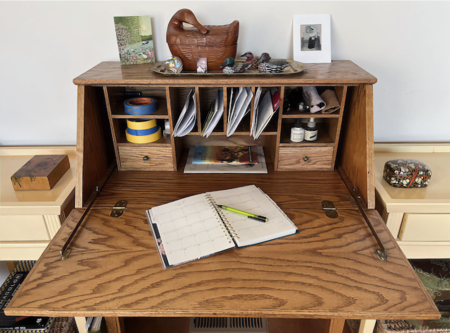 Photo of open oak desk, with open calendar and pen, and various objects in cubbyholes