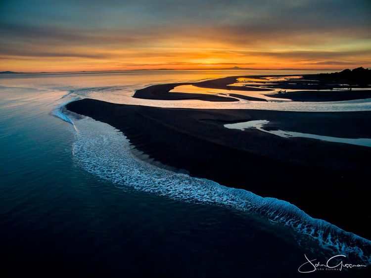 Photo of a red-orange sunrise over a river emptying into the ocean