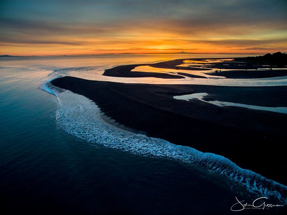 Photo of a red-orange sunrise over a river emptying into the ocean