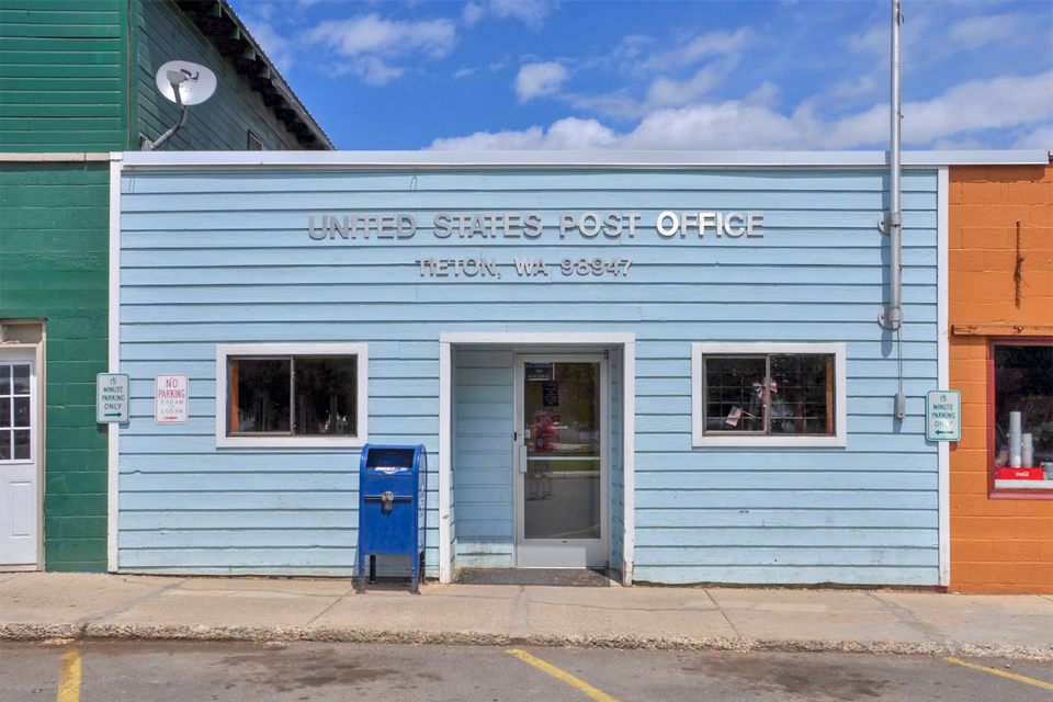 Photo of the front of a one-story blue building, with mailbox outside and "US Post office", and "Tieton WA 98947" on facade.