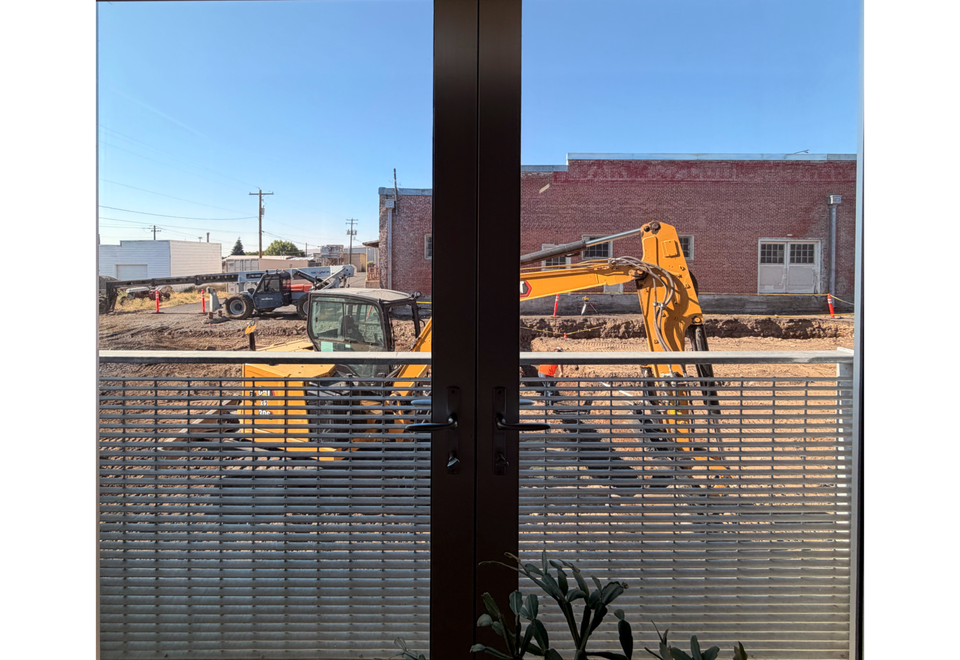Photo of a large orange backhoe through two French doors, on a torn up street.