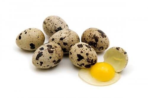 Speckled quail eggs with one cracked open, raw yolk and white spilling out, on a white background