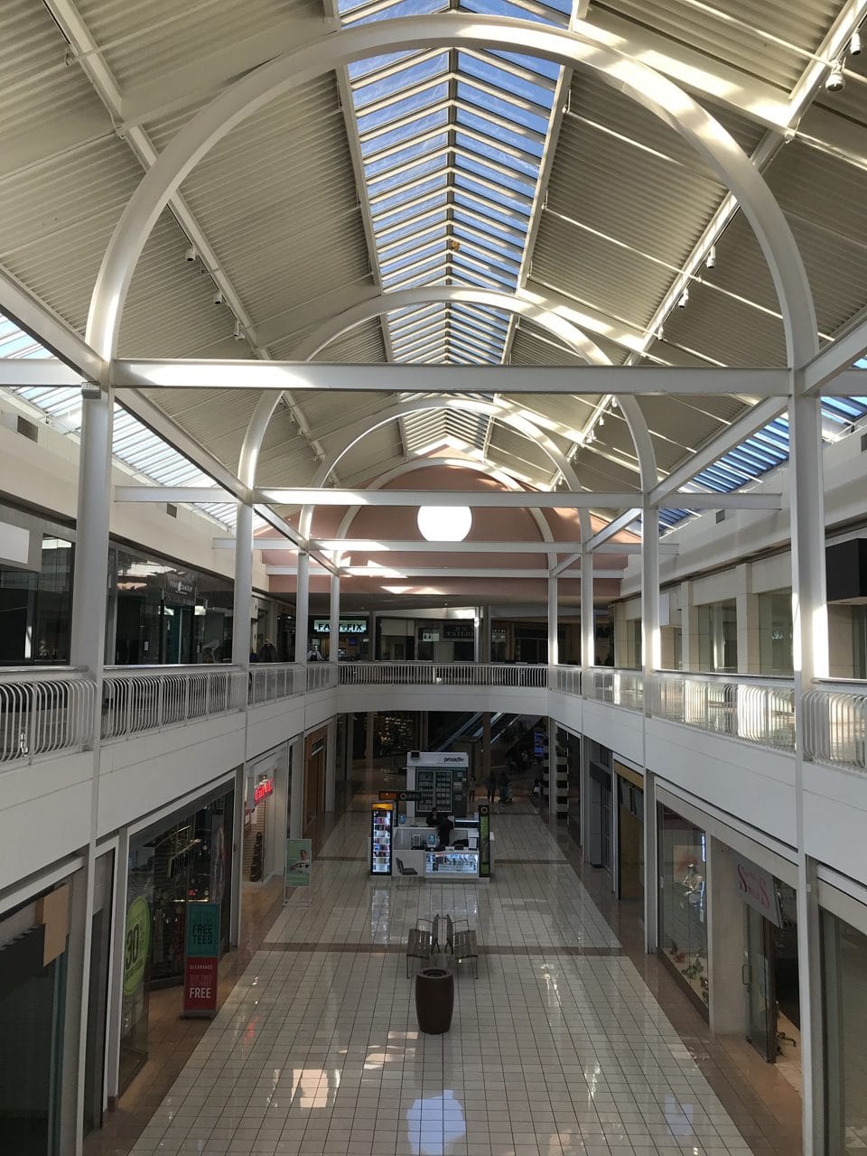Interior of an abandoned shopping mall with empty storefronts and still escalators, dead mall liminal imagery