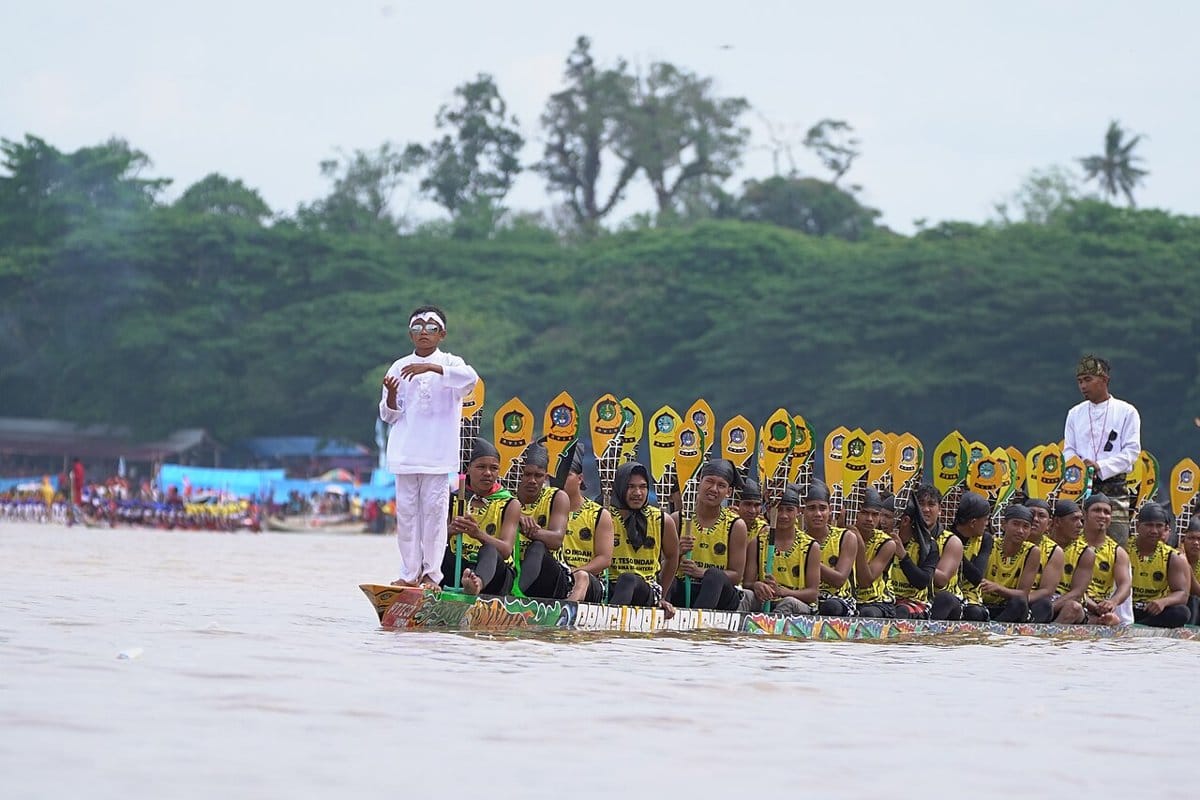 Long wooden racing boats crowded with rowers during a Pacu Jalur race in Riau, Indonesia