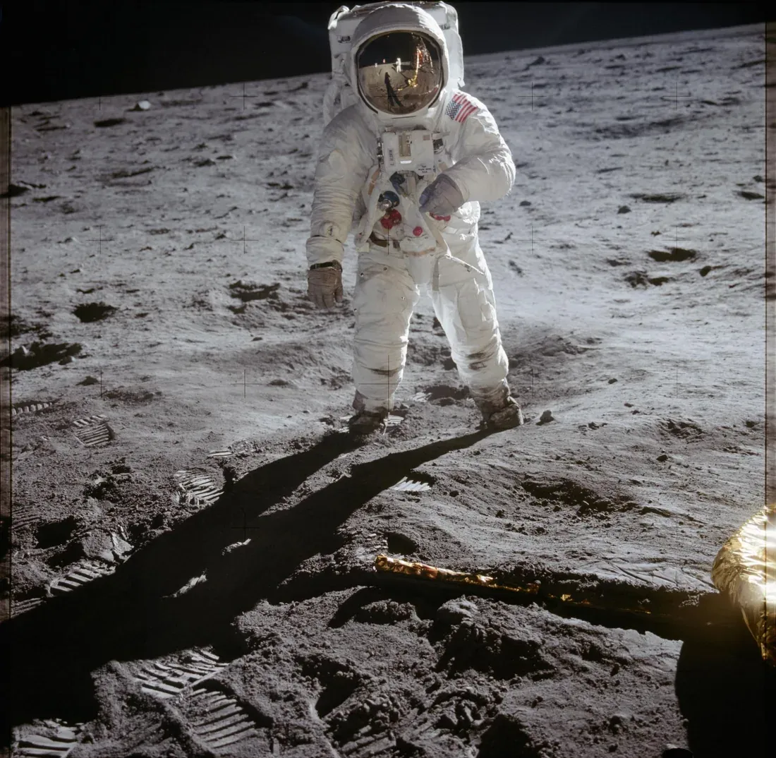 Apollo 11 astronaut on the lunar surface, reflective gold visor mirroring the lander and photographer