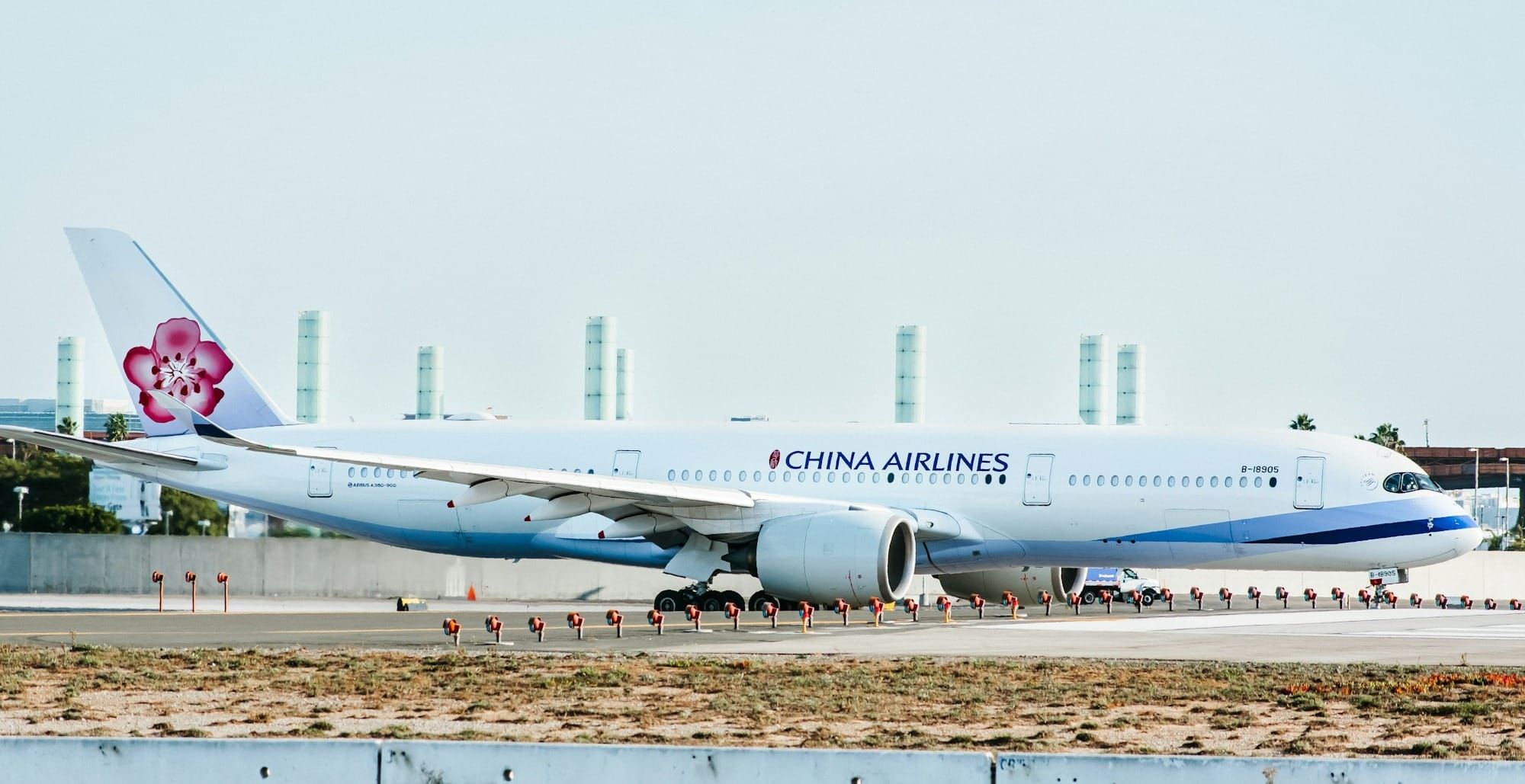 Photo of a large passenger airplane taxiing on runway with clear blue sky and airport terminal in background