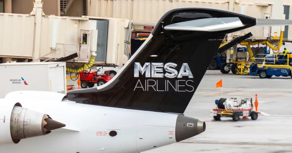 Photo of a modern airplane flying low over green fields with mountains in background and partly cloudy sky