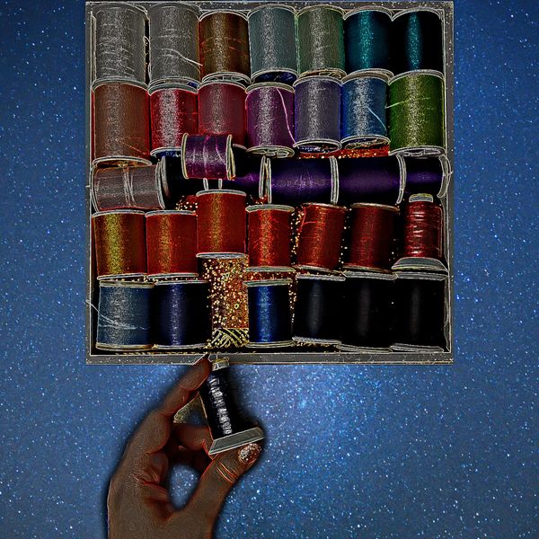 Box of different colored spools of thread with white hand holding one spool at the bottom. Blue space background.