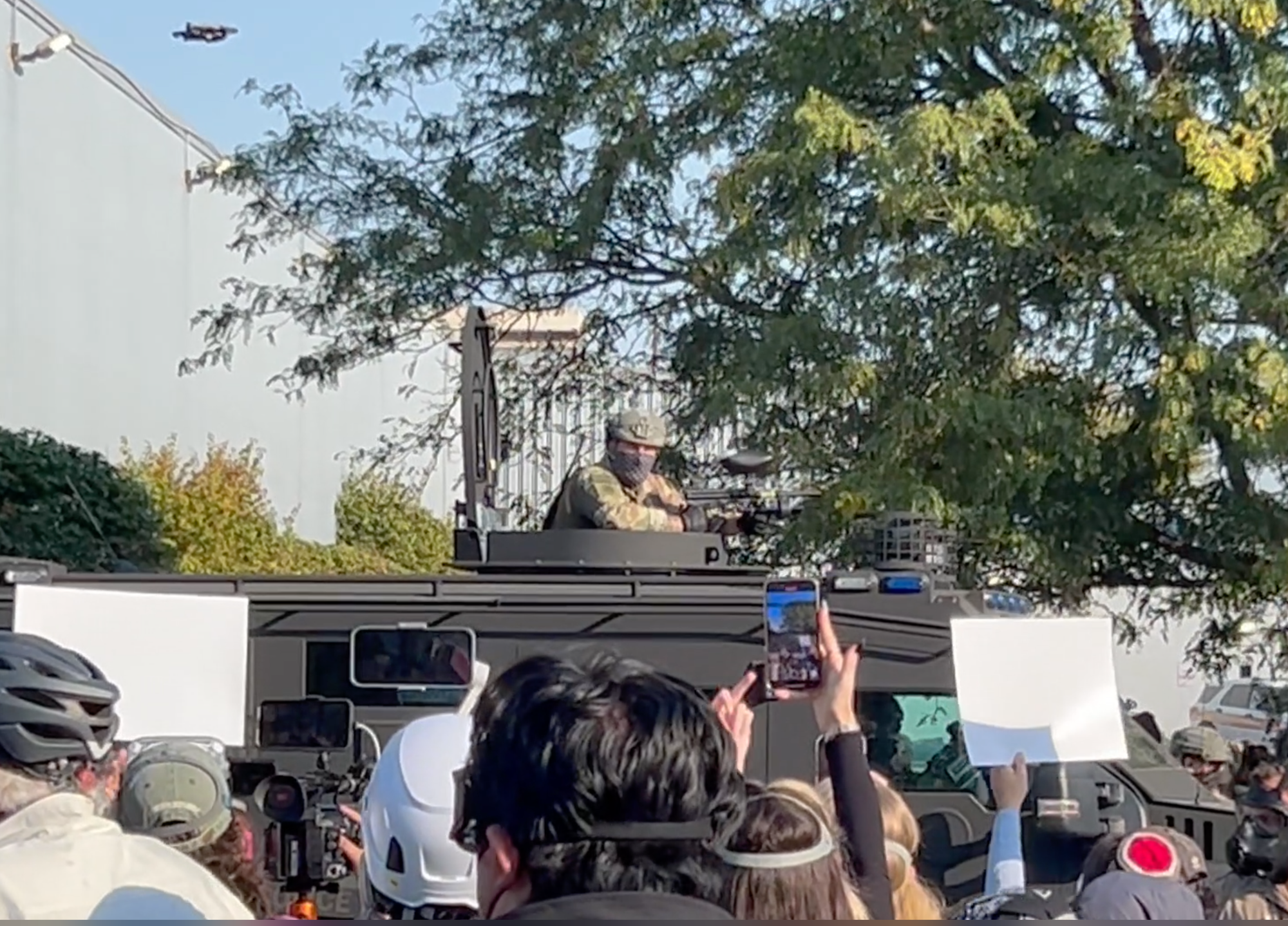 An ICE thug holding a gun, he is poking out the turret of a vehicle that is a cross between a tank and a jeep. 