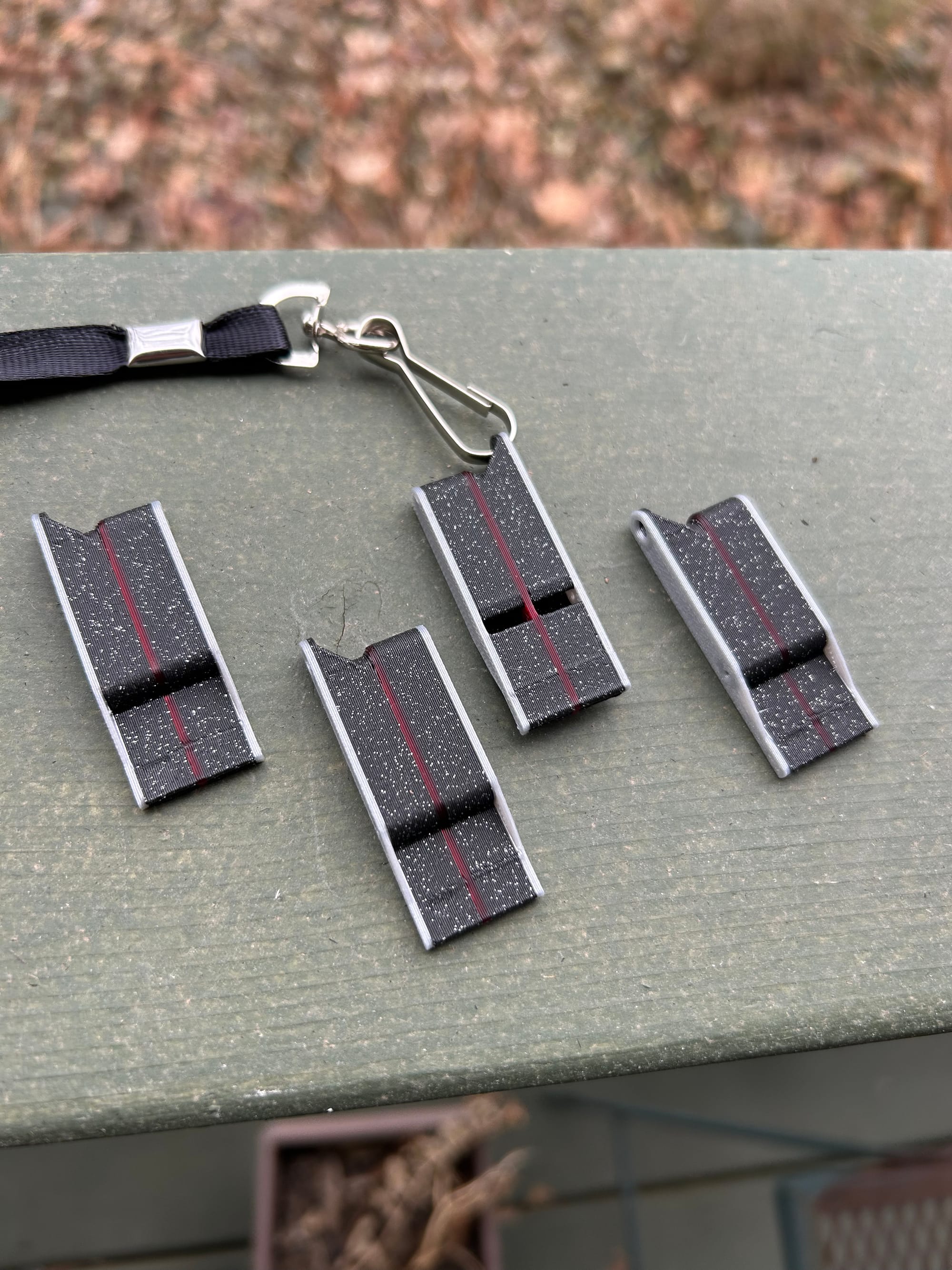 Four whistles with black bodies, grey trim and red stripes down the middle of each