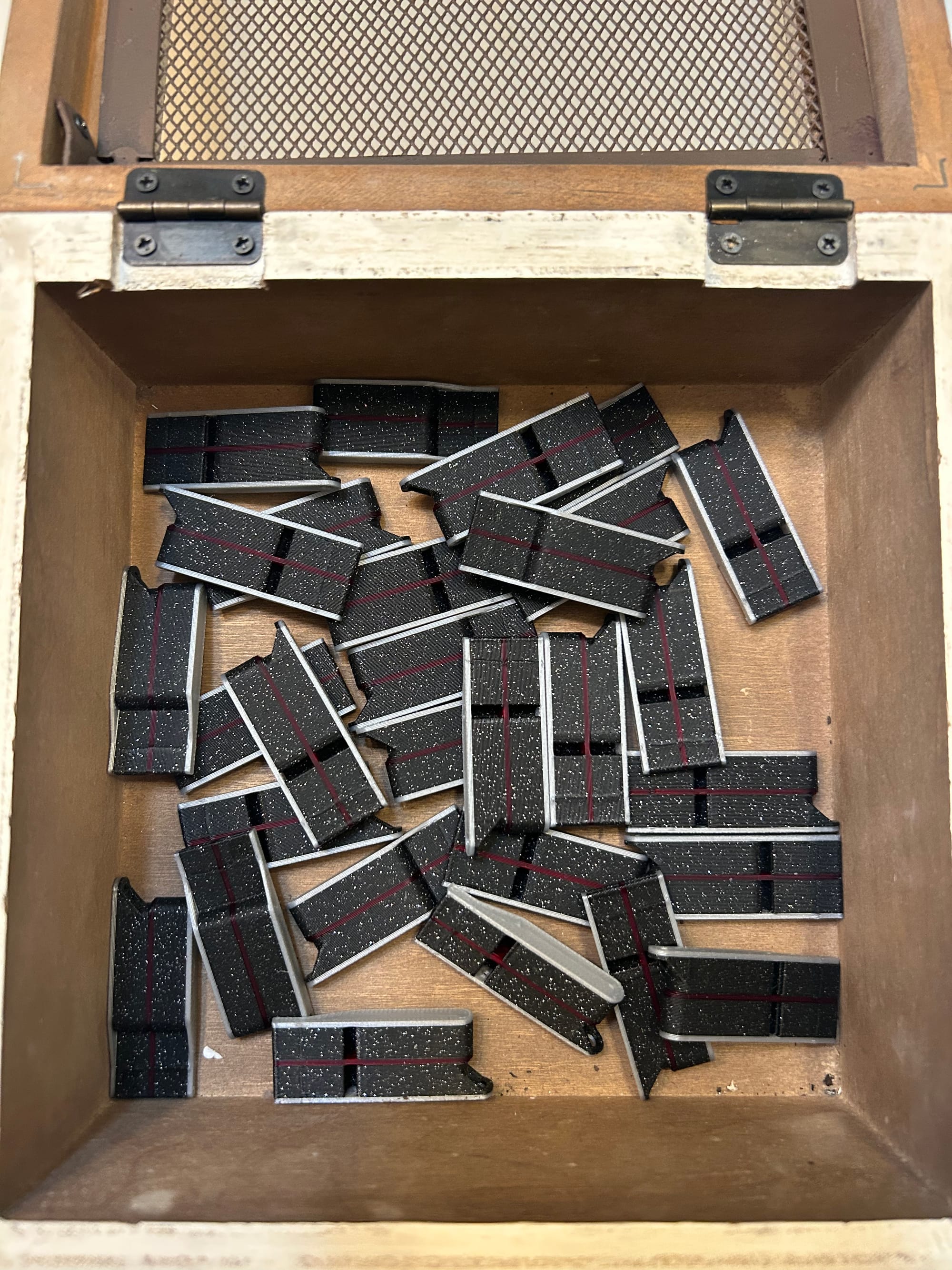 Many black rectangular whistles with red stripes in a wooden box