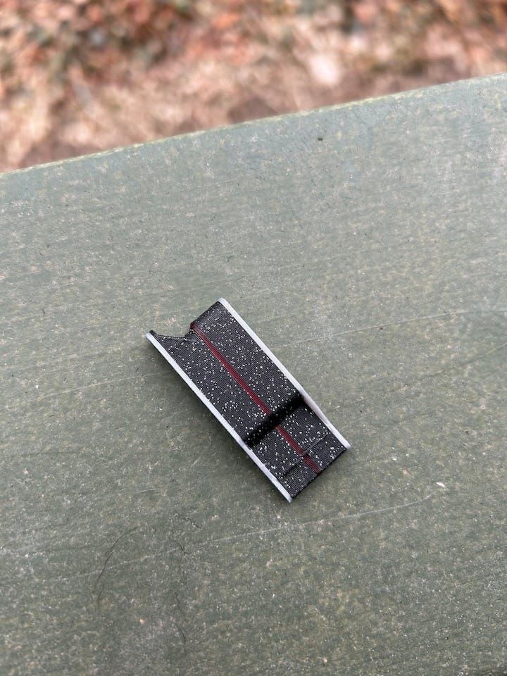a black rectangular whistle with a reddish purple stripe down the middle