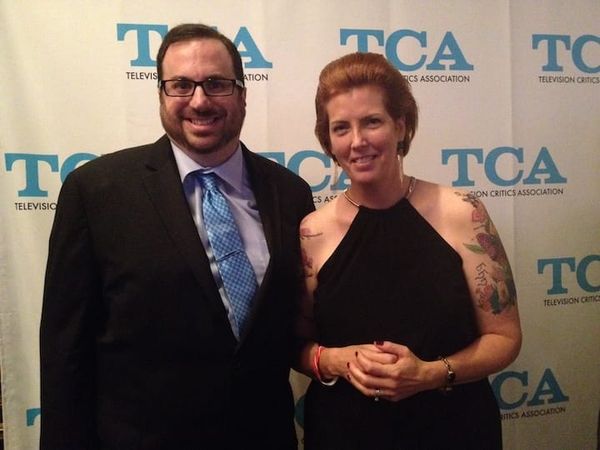 Alan Sepinwall and Mo Ryan at the T Awards in 2014. Alan wears a dark suit on the left, Mo wears a sleeveless dress on the right. both are smiling in front of a TCA Awards backdrop.