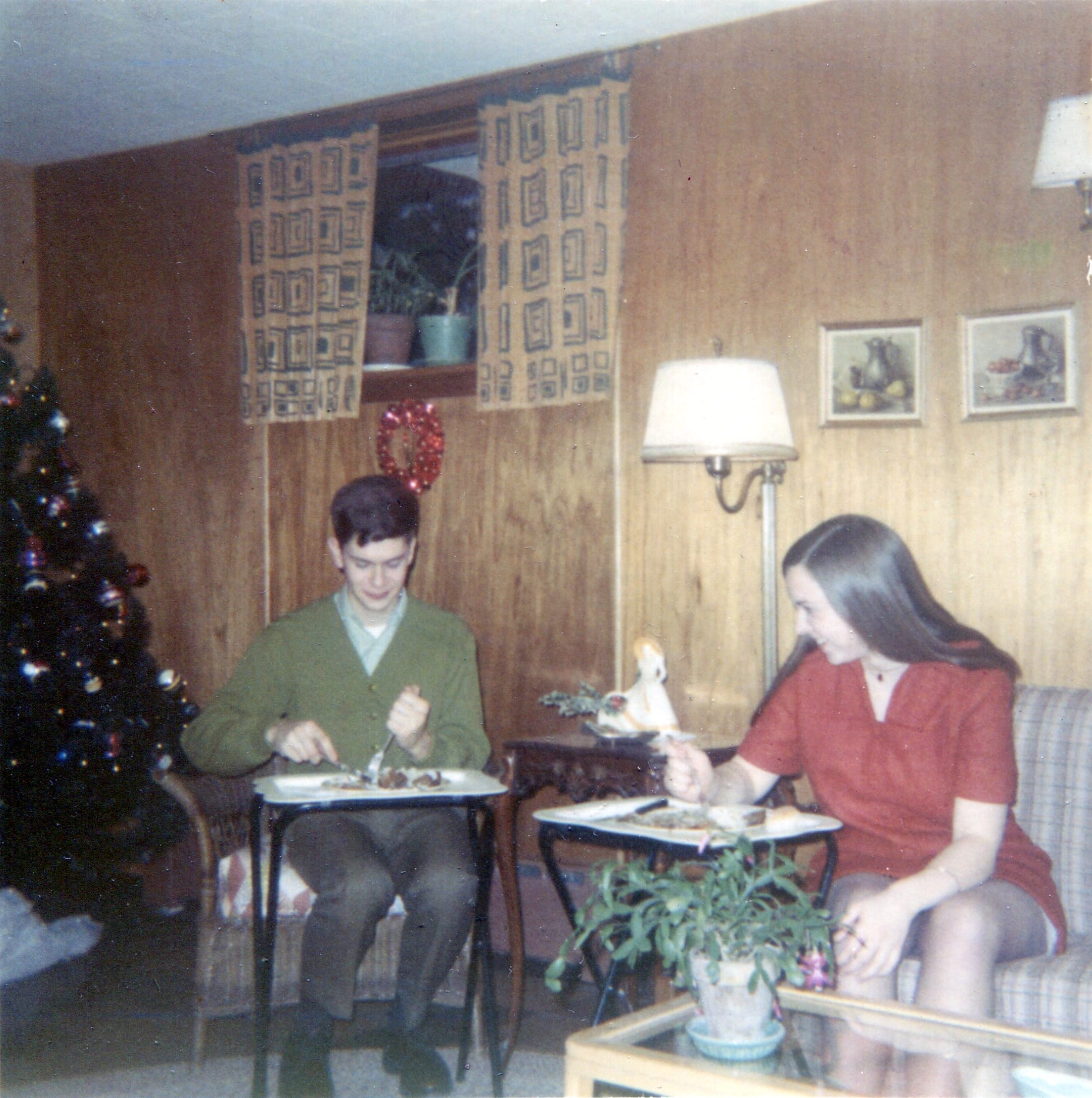 Two people eating dinner on TV tray tables in a home living room, circa 1970.