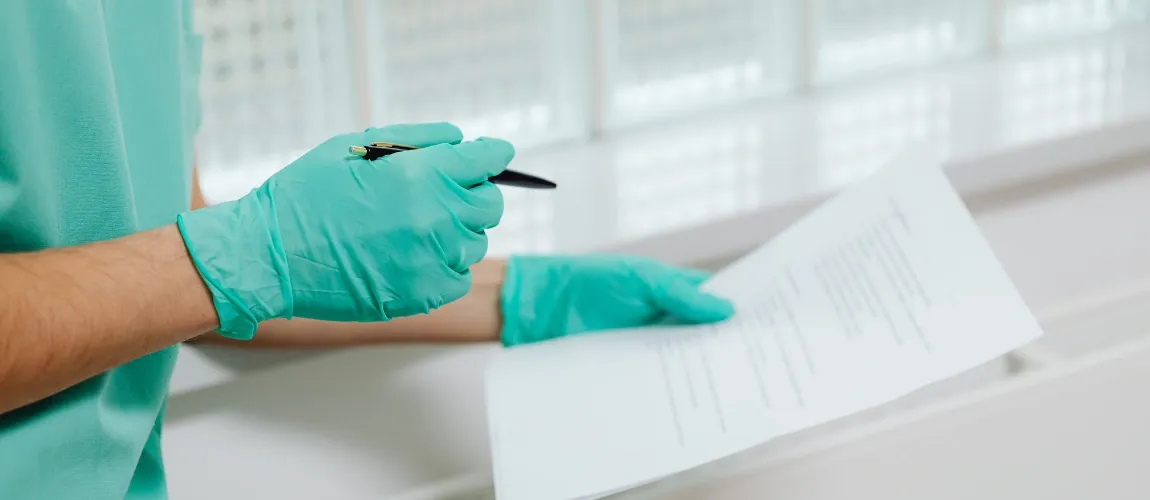 Eine Person mit Einmalhandschuhen hält einen Stift und ein Papier in der Hand.
