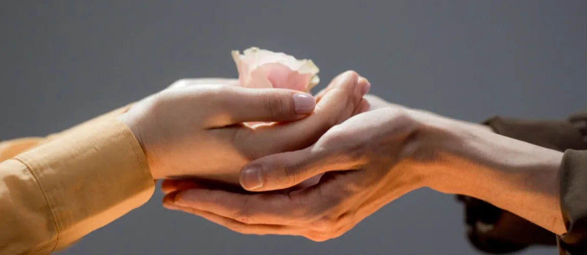 Eine Hand hält eine Blüte, eine andere Hand stützt sie.