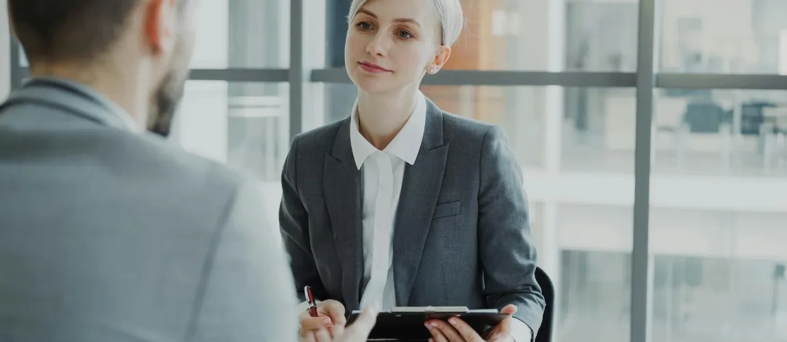 Eine Frau sitzt einem Mann mit Schreibmaterialien gegenüber.