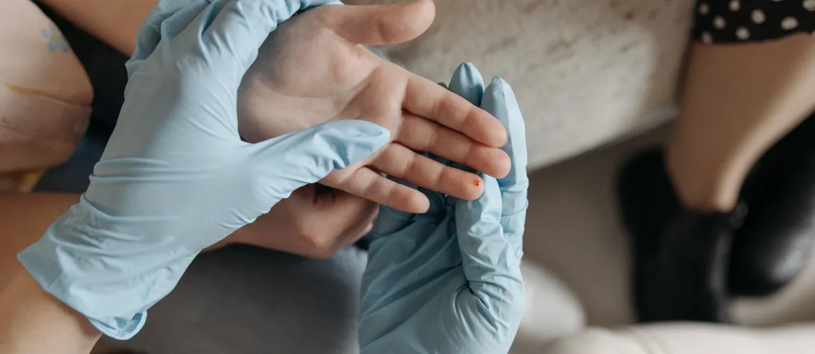 Eine Person mit Einmalhandschuhen bekleidet, hält eine Hand mit einem blutenden Finger. 