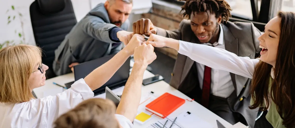 Fünf Personen strecken lächelnd die Fäuste zusammen. 