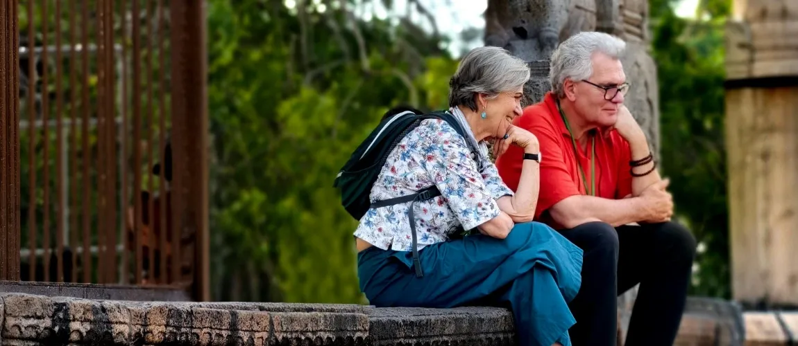 Zwei Senior:innen sitzen lächelnd auf einer Mauer. 