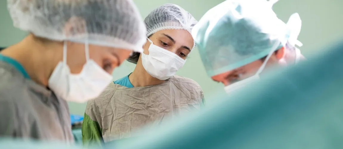 Drei Personen stehen mit OP-Kleidung im Operationssaal.