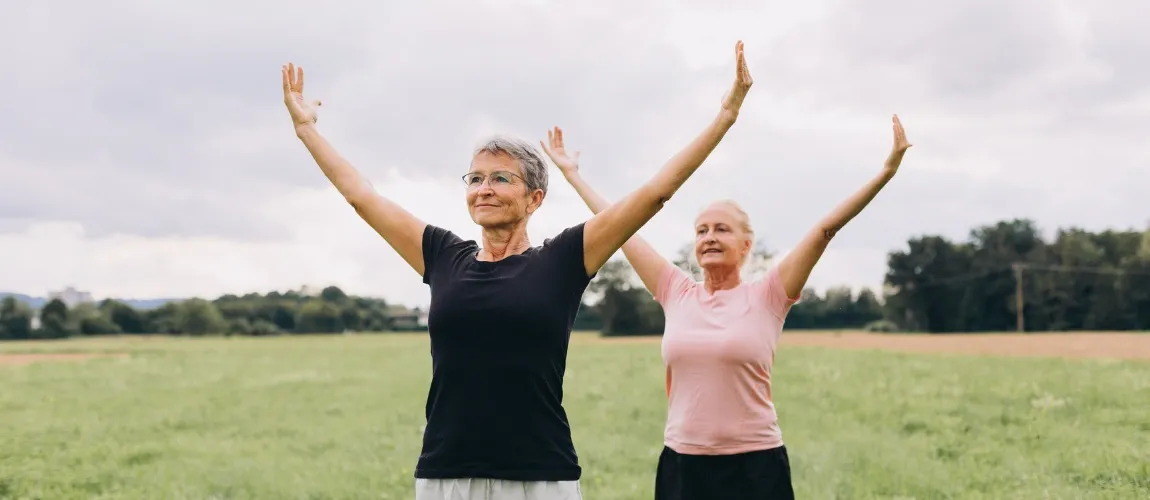 Zwei Seniorinnen machen Gymnastik im Grünen.