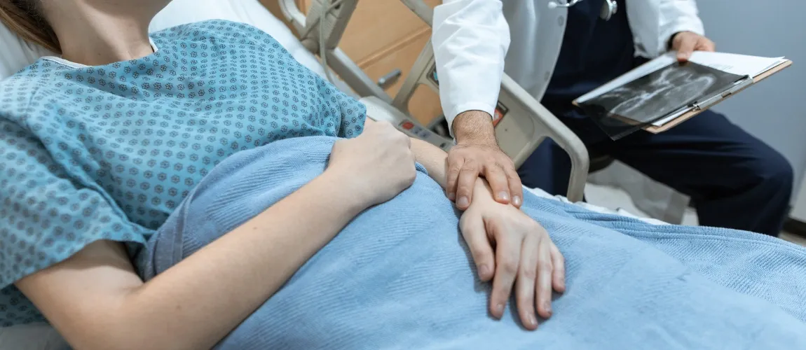 Ein Arzt legt einer Patientin im Krankenbett die Hand auf den Arm. 