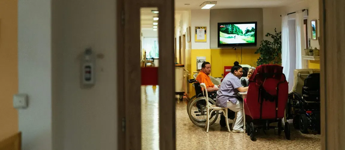 Altenpflegerin sitzt mit Patienten im Aufenthaltsraum.