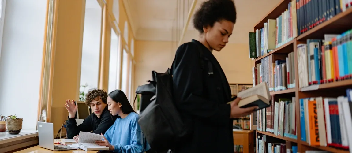 Eine Frau steht vor einem Bücherregal und liest in einem Buch.