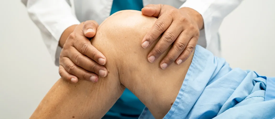 Ein Arzt untersucht das Kniegelenk eines älteren Patienten. 