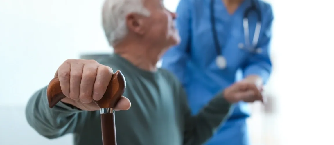 Eine Pflegekraft hilft einem Patienten aufzustehen. 
