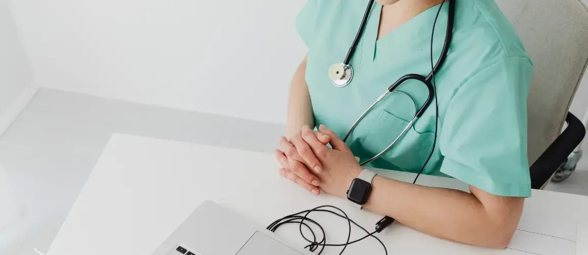 Pflegekraft sitzt am Schreibtisch vor dem Laptop.