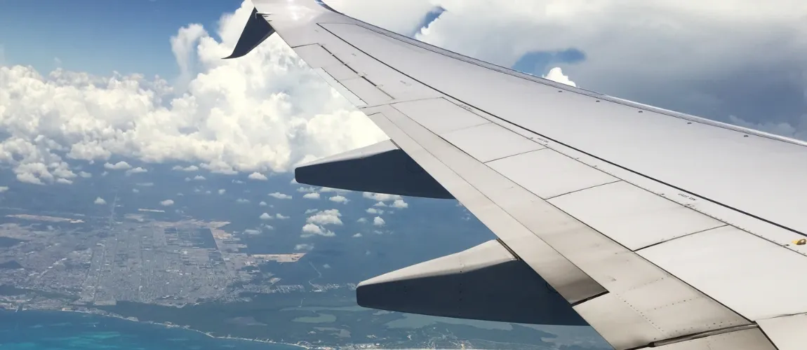 Nahaufnahme eines Flugzeugflügels mit Wolken und Landschaft im Hintergrund.