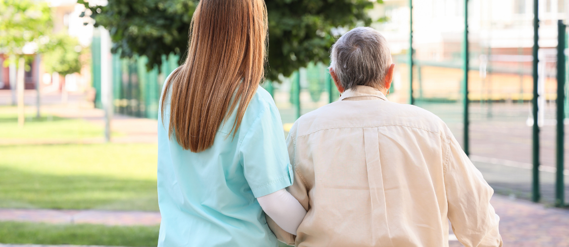 Eine Pflegekraft geht mit einer Patient:in spazieren. 