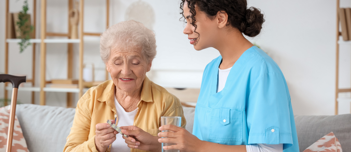 Eine Pflegekraft reicht einer älteren Patientin Medikamente an. 