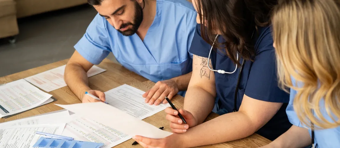 Drei Pflegeauszubildende sitzen am Tisch mit Lernmaterial.