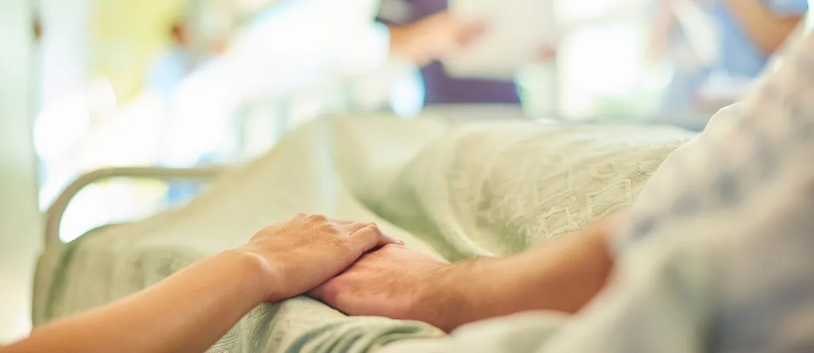 Eine Besucherin hält die Hand eines Patienten. 