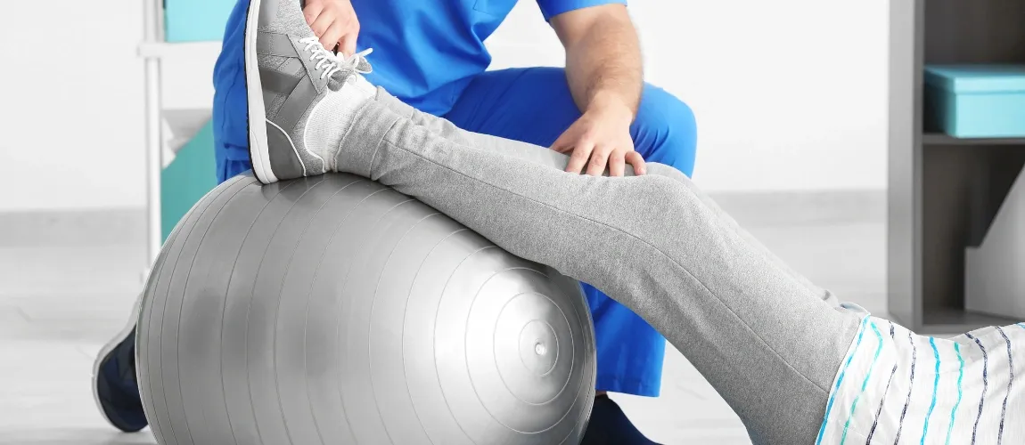 Eine Patientin macht Übungen mit einem Ball gemeinsam mit einem Pfleger. 