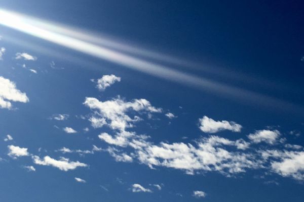 Cielo blu con piccole nuvole attraversato da una striscia di luce
