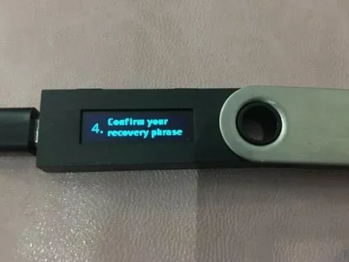 Pantalla del dispositivo Ledger indicando confirmar la frase de recuperación y seleccionar una palabra