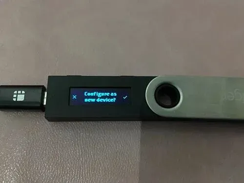 Pantalla del Ledger Nano S indicando “Configurar como nuevo dispositivo”, con el cursor apuntando a la opción derecha “Configurar como nuevo dispositivo”