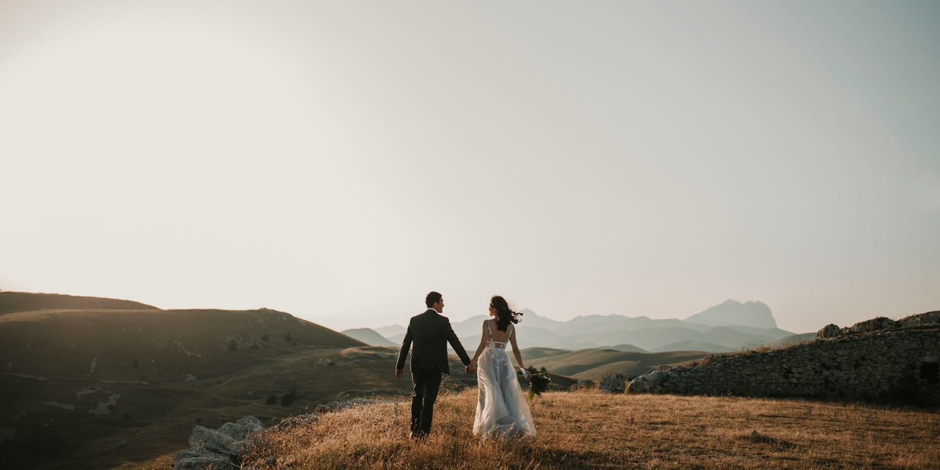 a bride and groom walking on a hill