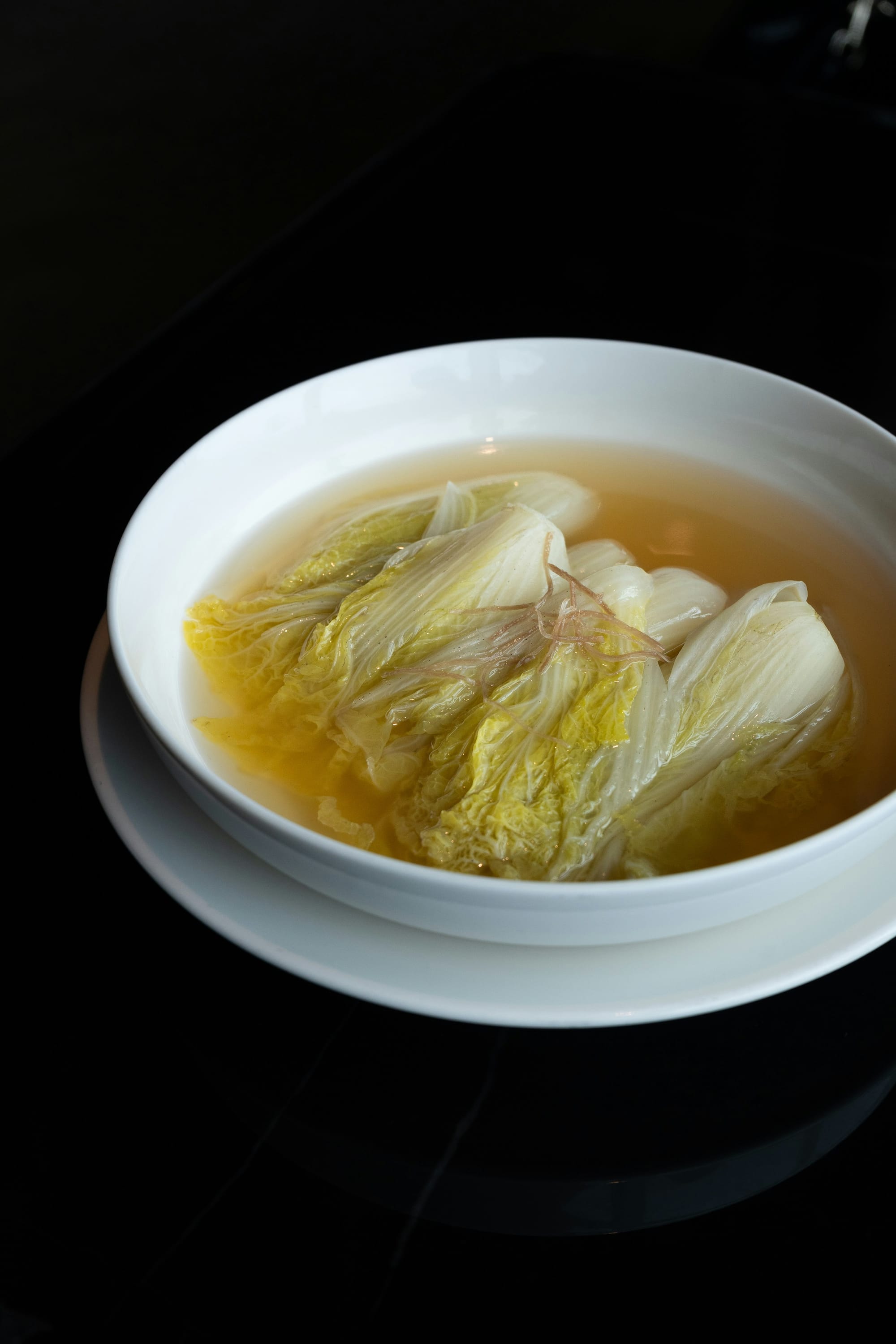 Traditional Sichuan Cabbage in Supreme Broth (Kaishui Baicai) served in a shallow white bowl showing tender cabbage hearts submerged in crystal-clear consommé.