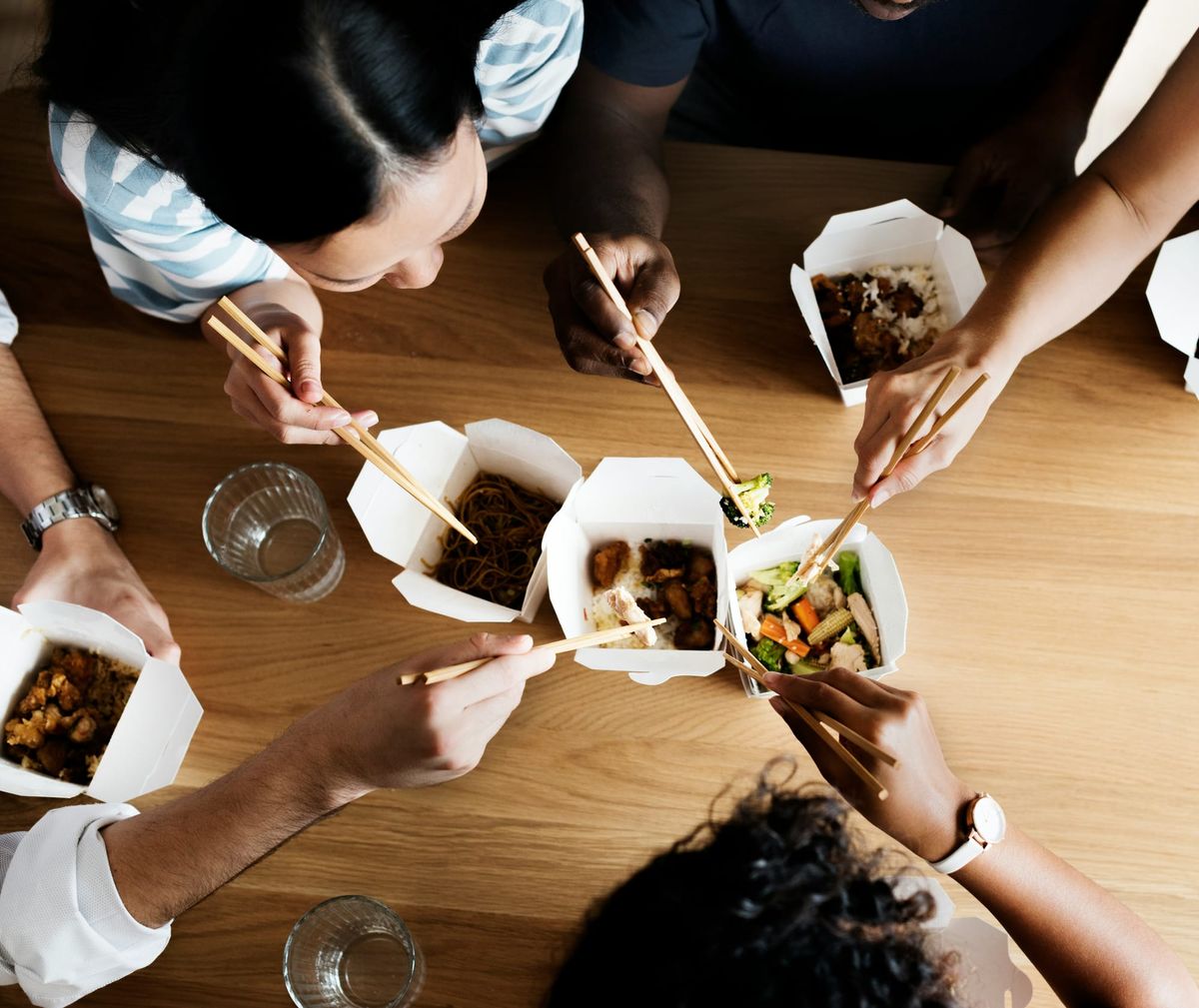 A group of friends eating Western-style Chinese food from classic white paper boxes using chopsticks