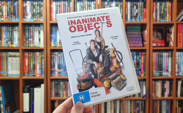 The DVD for Inanimate Objects. A man and woman surrounded by junk: an old skateboard, typewriter, rusty applicances. Behind the DVD is a wall of physical media.