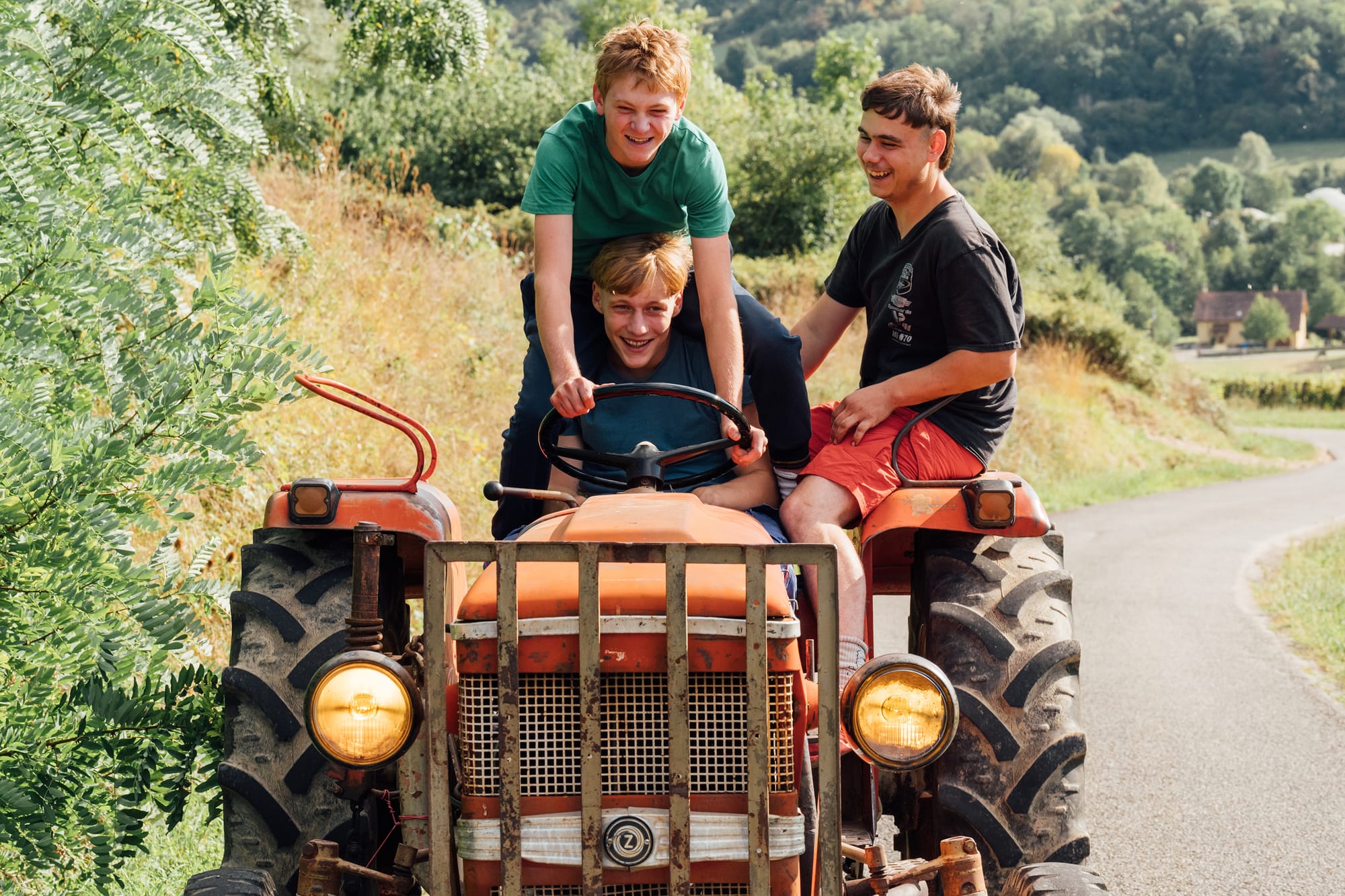 Three laughing young men on a tractor in the countryside.