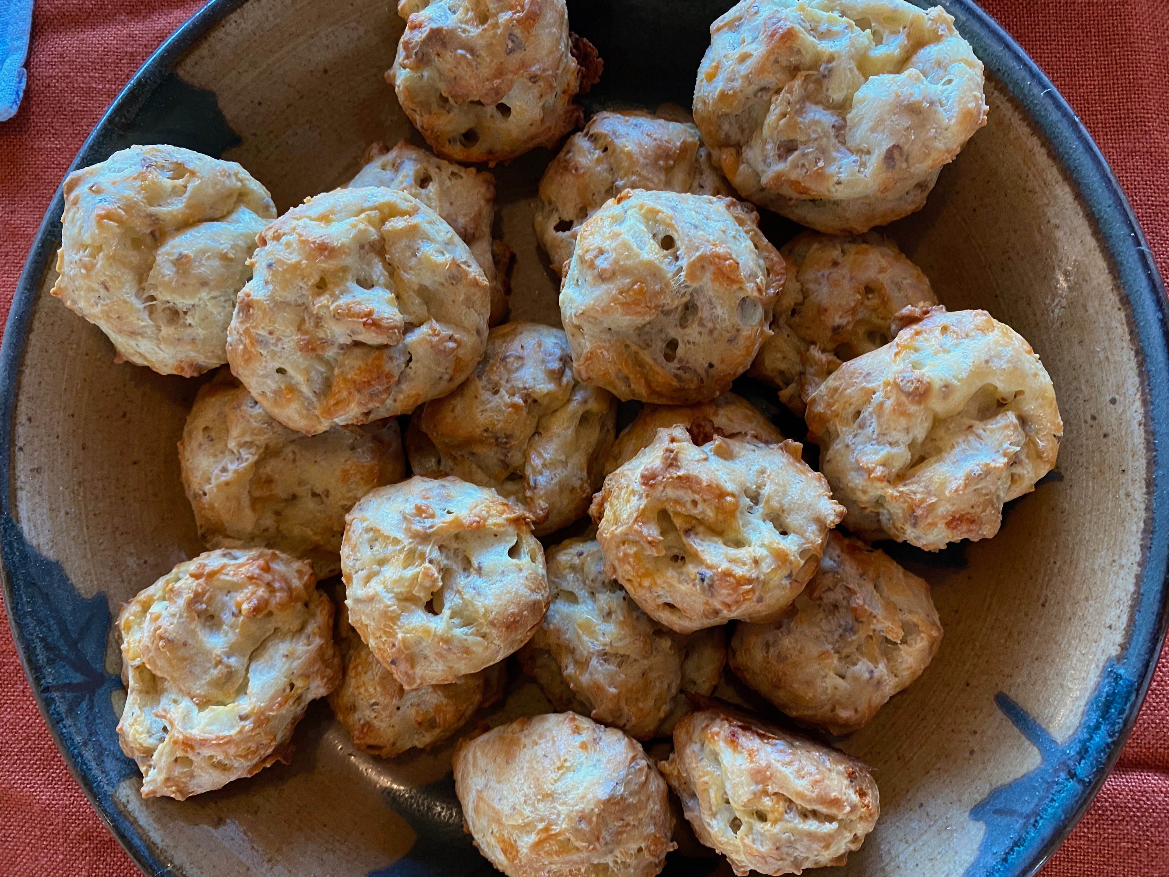 A ceramic bowl filled with a pile of small, round cheese puffs, craggy and uneven with browned tops.