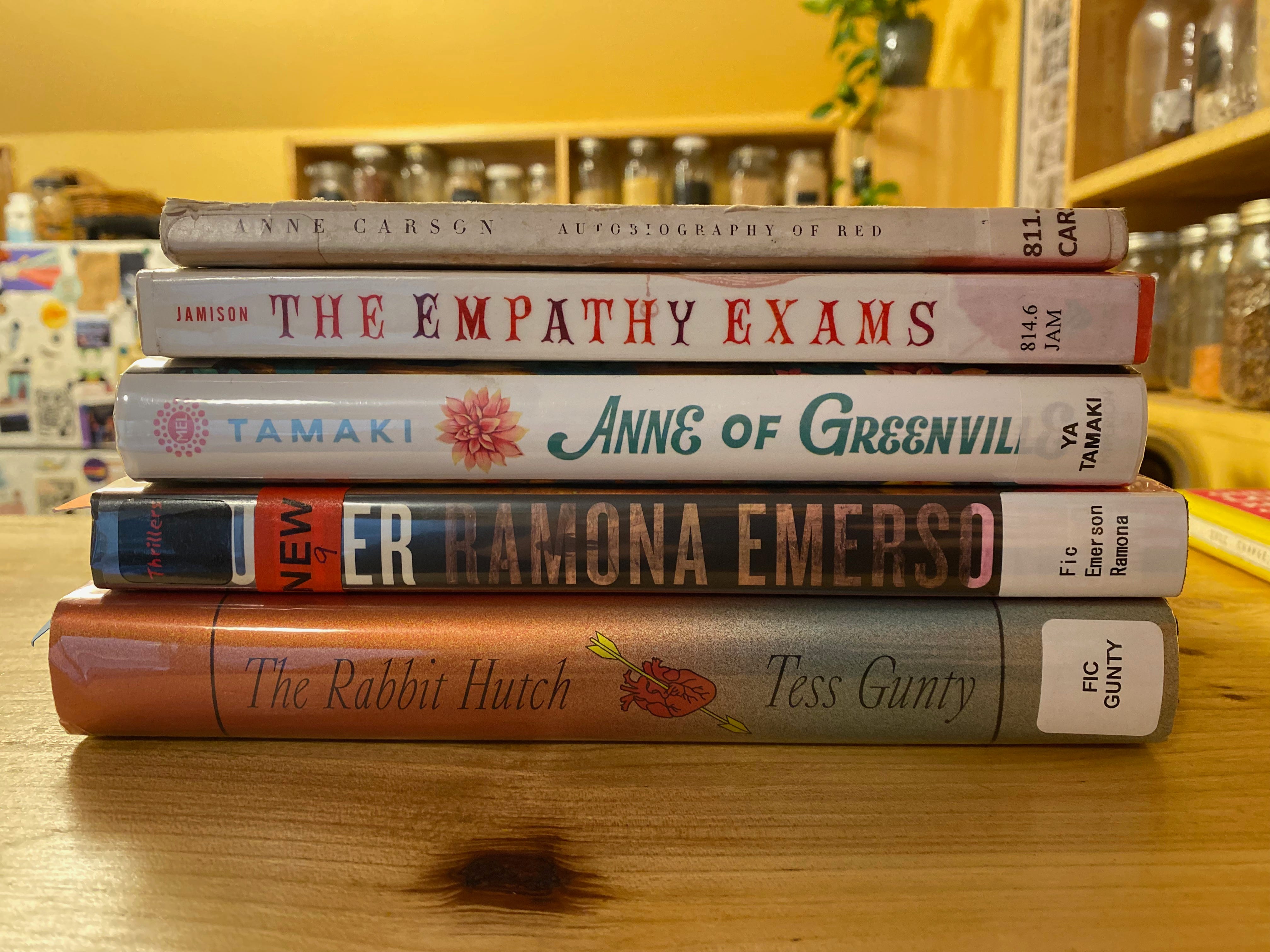 The five listed books stacked on a wooden counter with kitchen shelves and a fridge visible in the background.