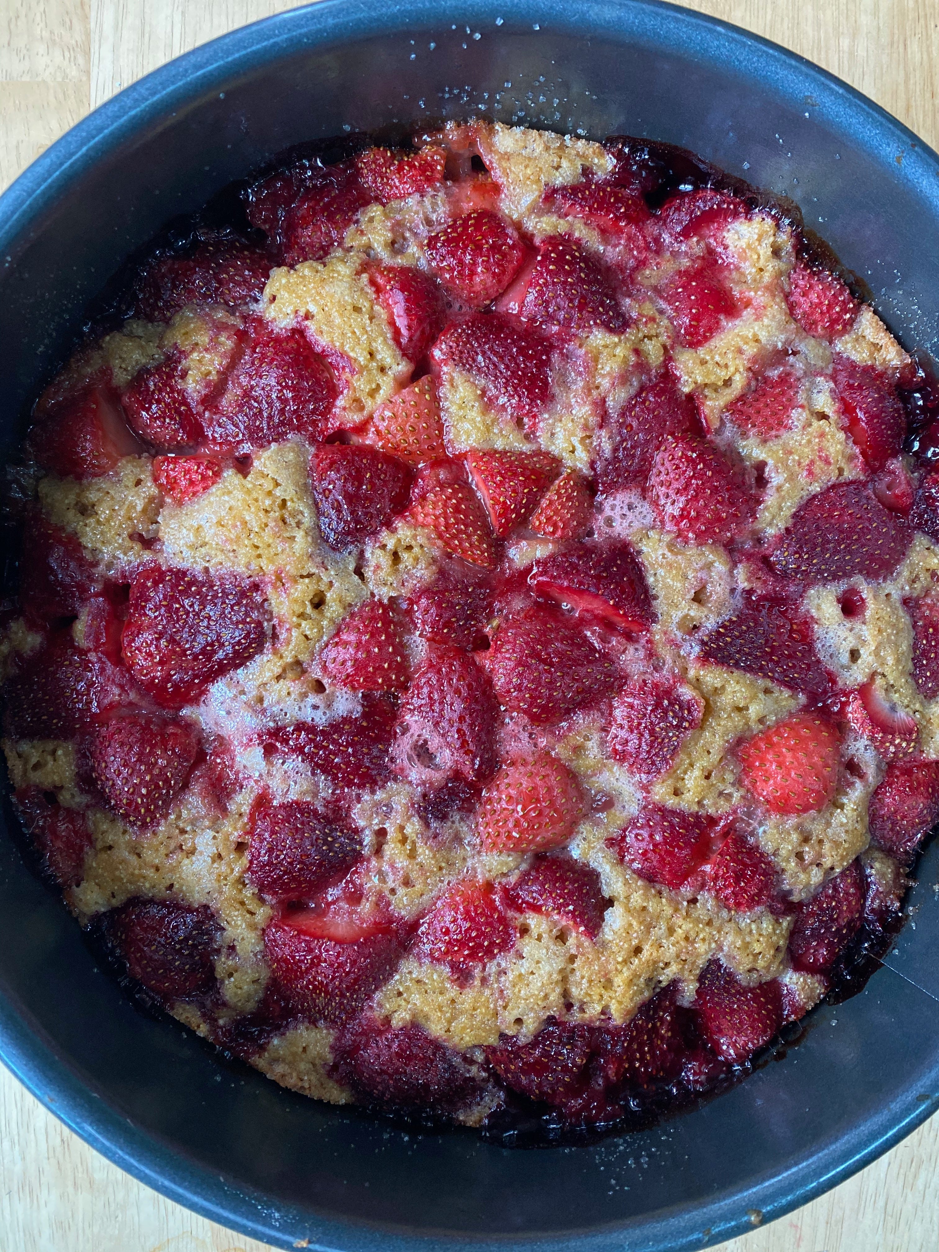 A closeup view of a strawberry cake in a springform pan. The top is golden brown and studded with strawberry halves.